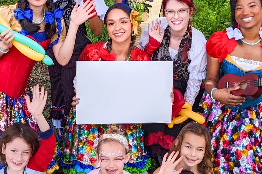 Happily Ever Laughter party faeries in costume with children at an outdoor event, one faerie holding a sign