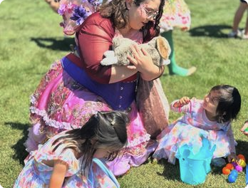 A Happily Ever Laughter faerie holding a small child while another child sits nearby on a lawn.