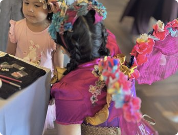 A faerie performer in a pink costume with a young child at an indoor event.