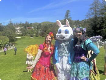 Two Happily Ever Laughter faeries and a person in an Easter bunny costume on a golf-course lawn.