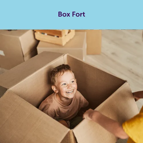 A smiling child sitting inside a cardboard box, creating a fun and imaginative box fort activity for a rainy day party.