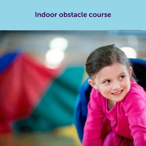 A smiling child in a pink sweater enjoying an indoor obstacle course, a fun and active solution for a rainy day party.