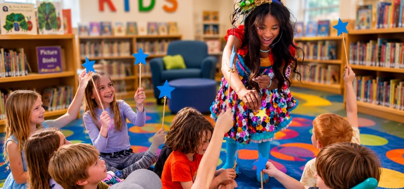 A character performer leading a group of children through a reading-themed activity at a library.