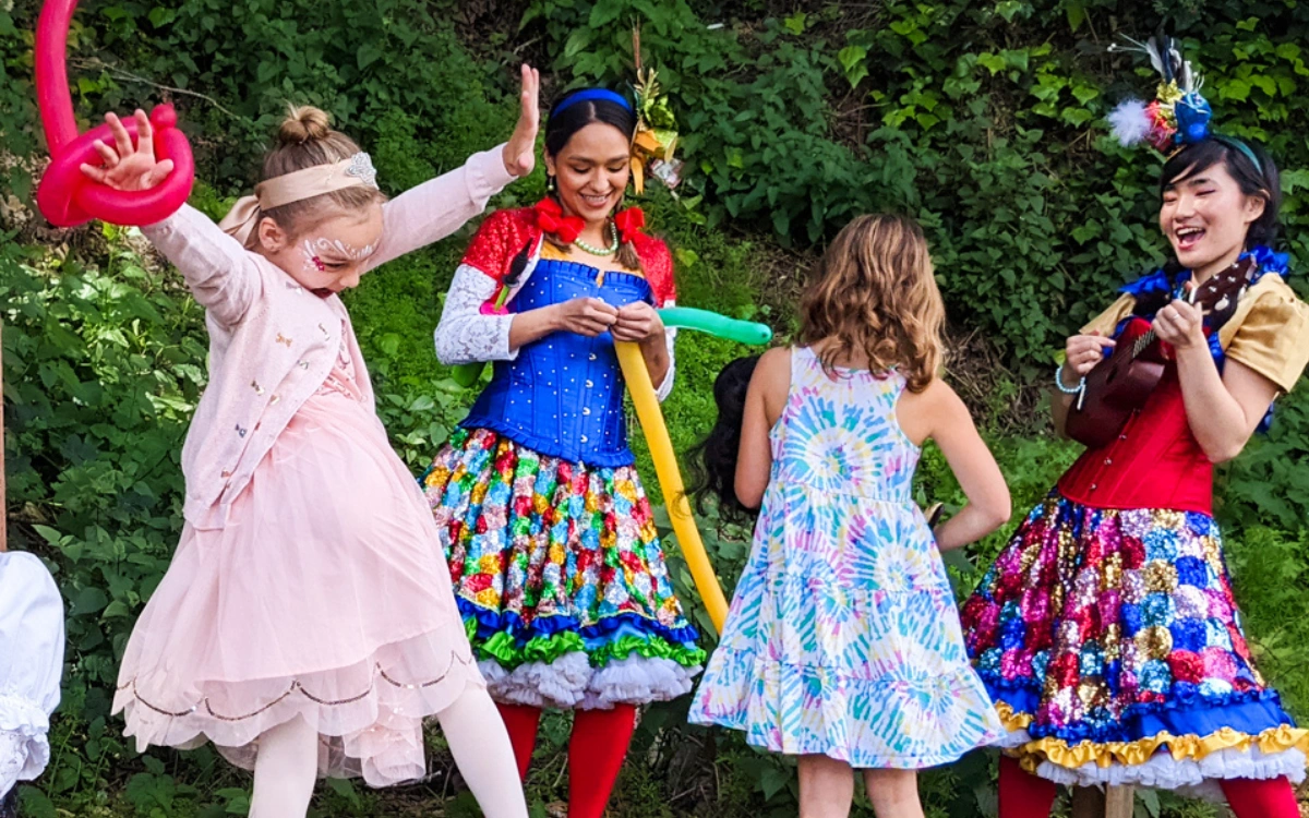 Costumed Happily Ever Laughter entertainers leading a line of children in a game at a party.
